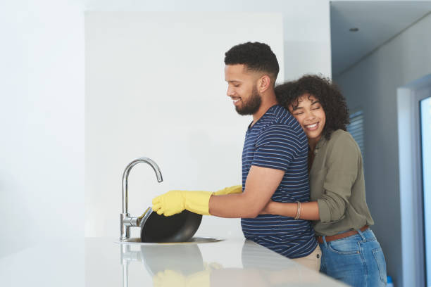 Shot Of A Young Man Washing The Dishes While His Wife Hugs Him At Home